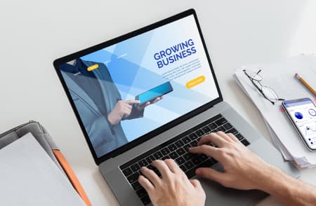 otwarty laptop ze stroną o rozwoju biznesu, na klawiaturze widać ręce ustawione do pisania